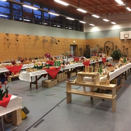 In einer Turnhalle sind mehrere Tische mit Auststellungsstücken aus Holz und Metall aufgestellt.