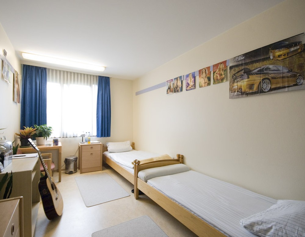 Ein Patientenzimmer mit zwei Betten. an der Wand hängen Bilder und Poster.