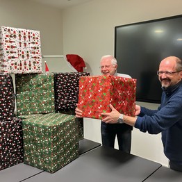 Zwei Männer halten lachend Weihnachtspakete in den Händen.